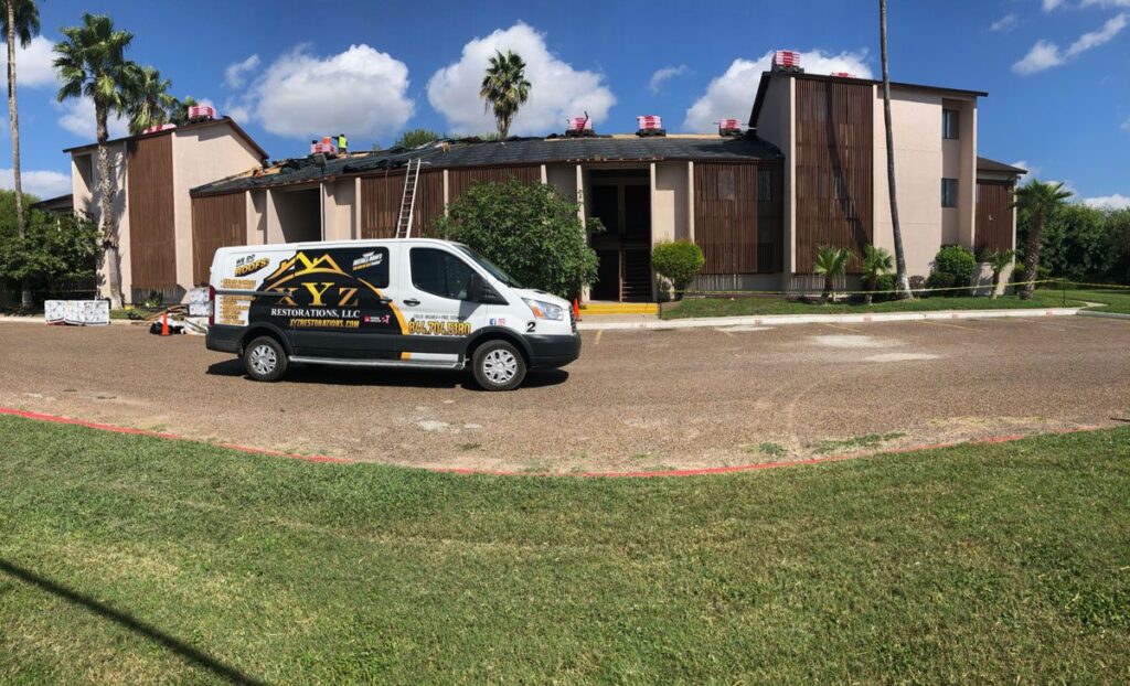 Exterior of brown building with a van of a roofing company brownsville.|Top of a home that with working giving restoration services brownsville.